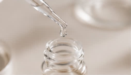A dropper releasing a bead of serum over an open glass bottle
